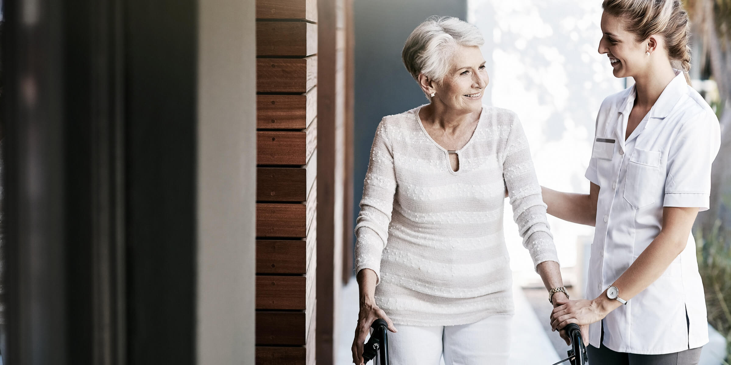 Bild zeigt eine junge Pflegerin und eine Seniorin mit Laufhilfe