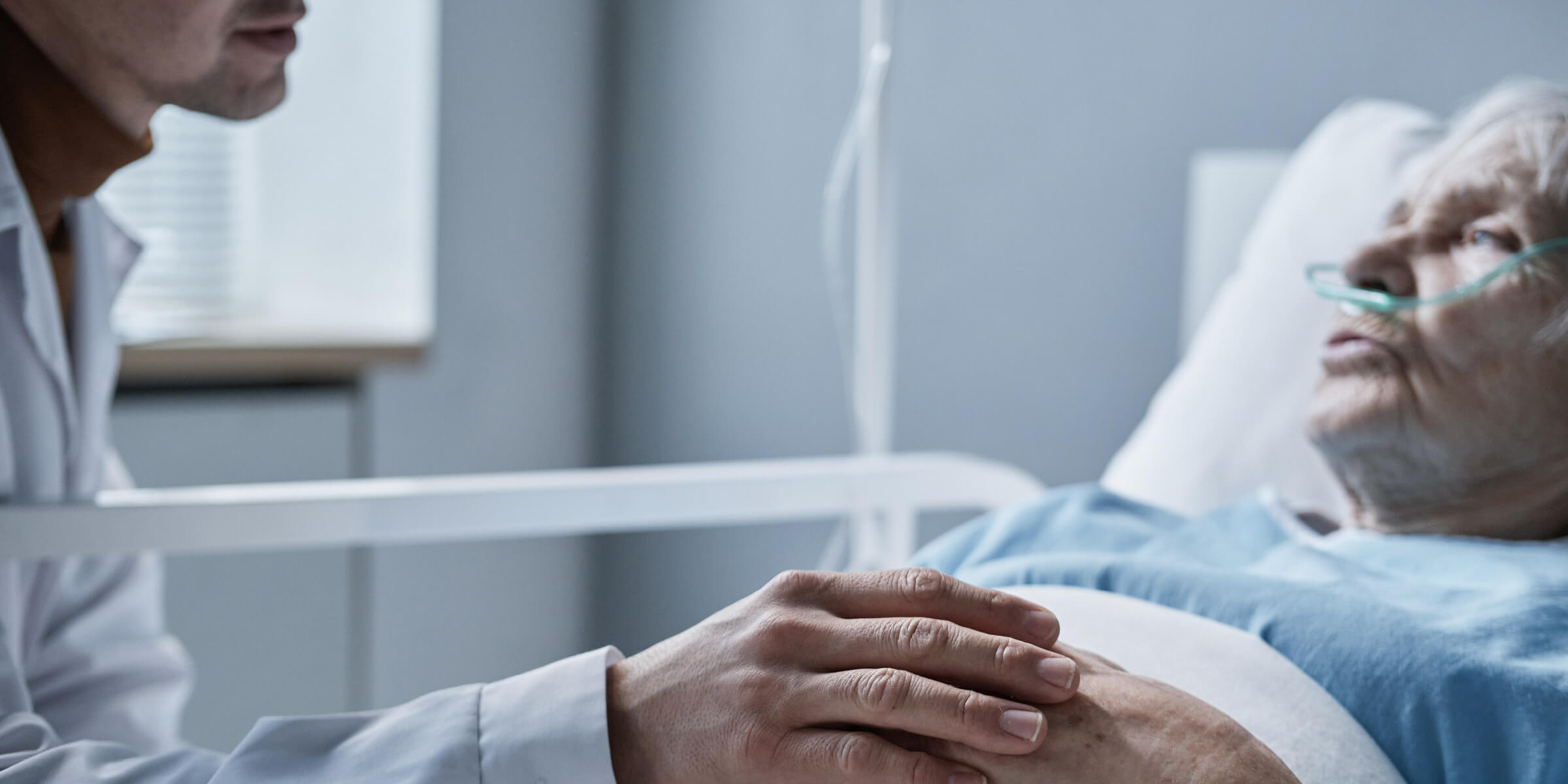 Bild zeigt eine Nahaufnahme eines Arztes, der die Hand einer älteren Frau hält, während sie auf dem Bett liegt, er unterstützt sie während ihrer Krankheit