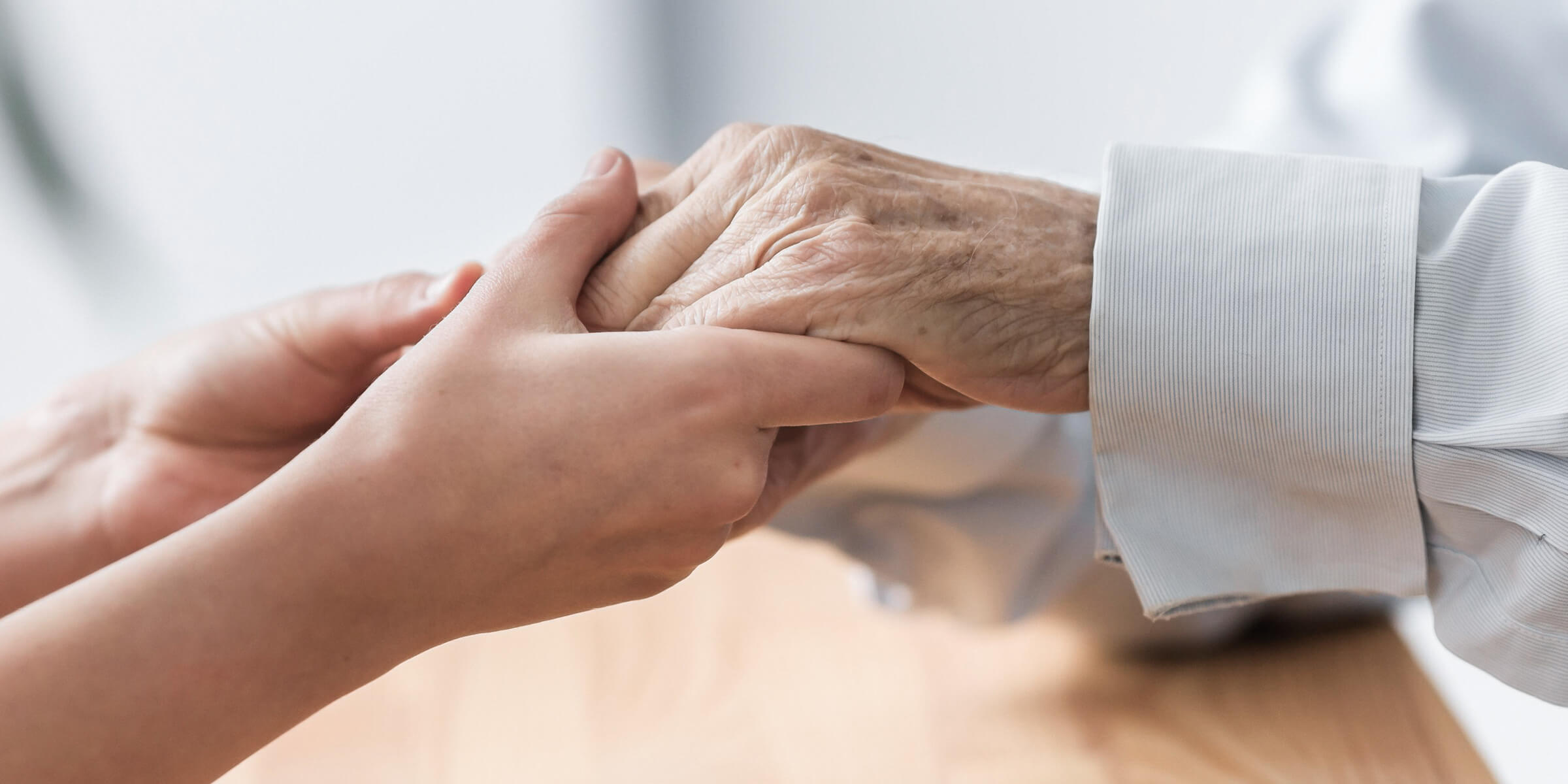 Bild zeigt wie eine Krankenschwester die Hände eines älteren Patienten hält.